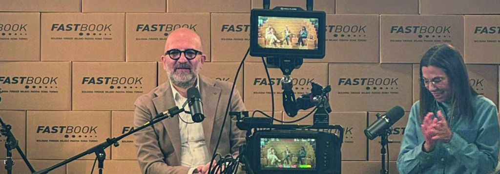 Intervista Donato Carrisi di Elizabeth Cappa davanti a uno sfondo di scatole targate Fastbook