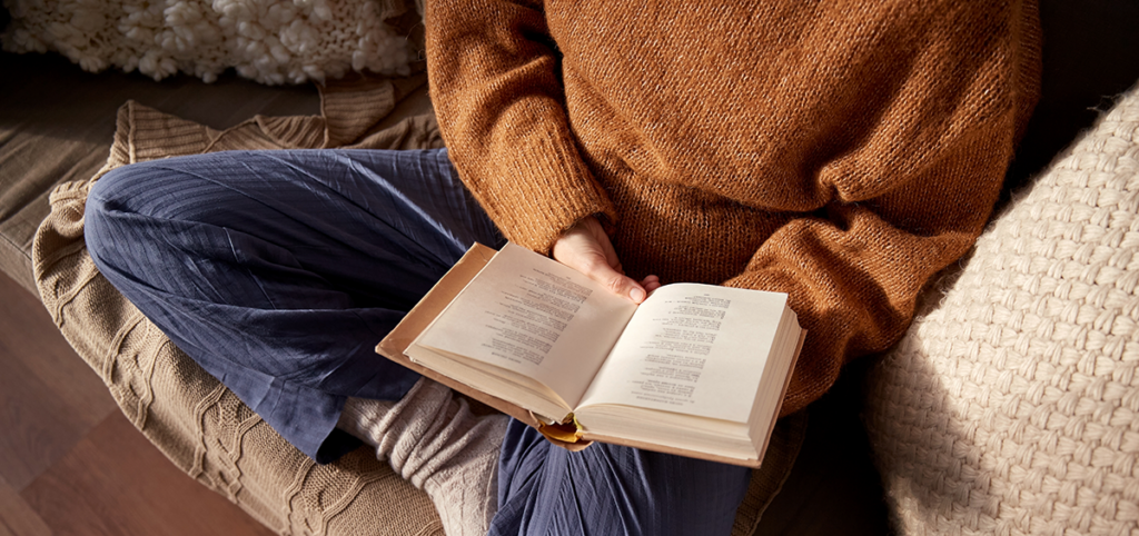Novità libri gennaio 2026. Ragazza a gambe incrociate su un divano con un libro aperto in mano. la parte superiore della ragazza è tagliata