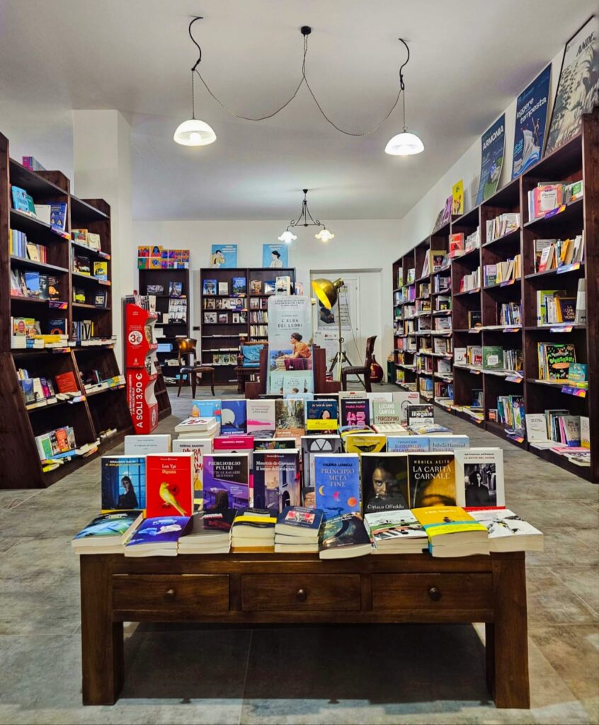 Interno della libreria Idrusa di Alessano con un tavolo cenntrale e pareti a lato